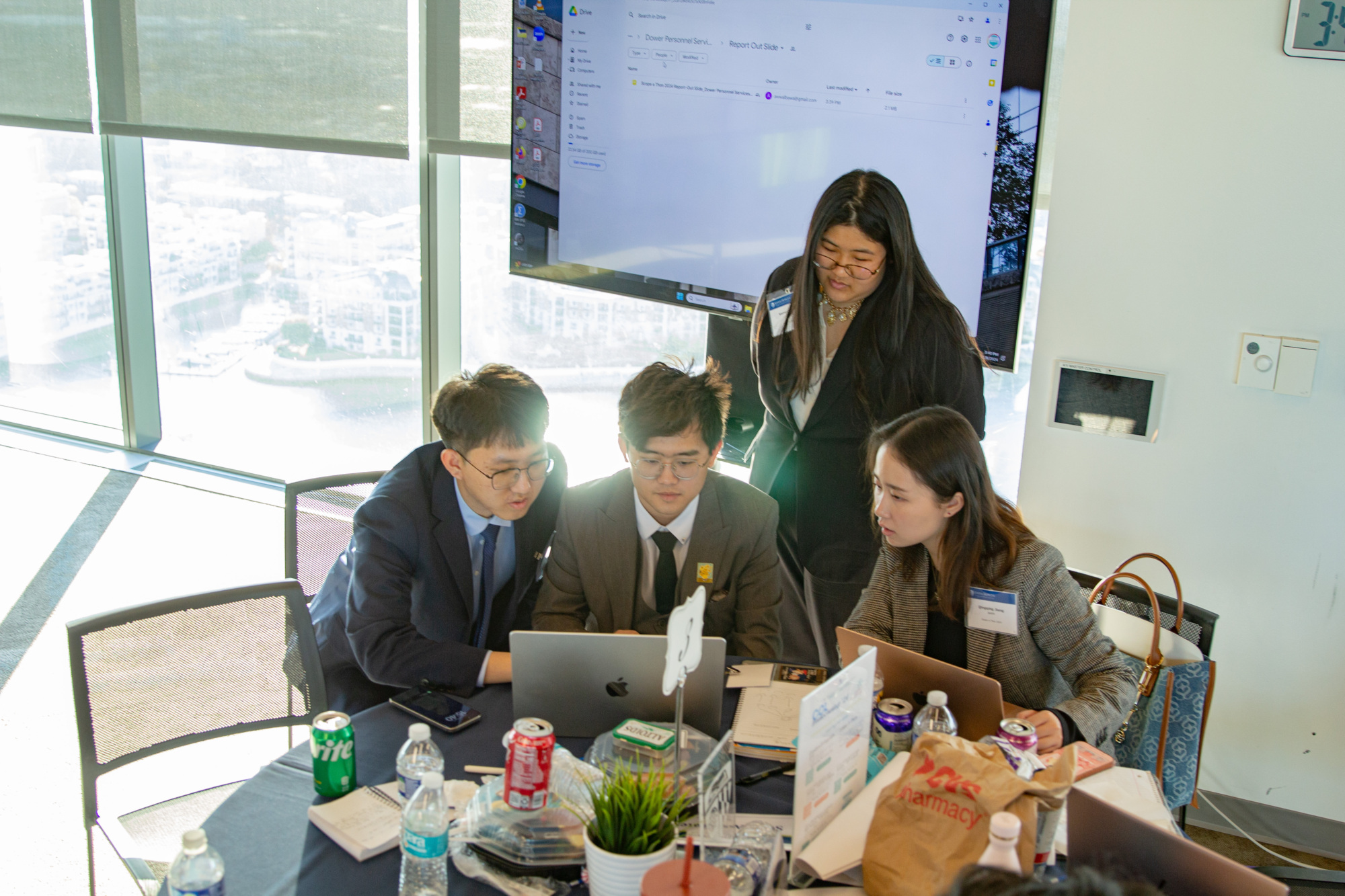 people working at a table with someone standing over them looking at a laptop