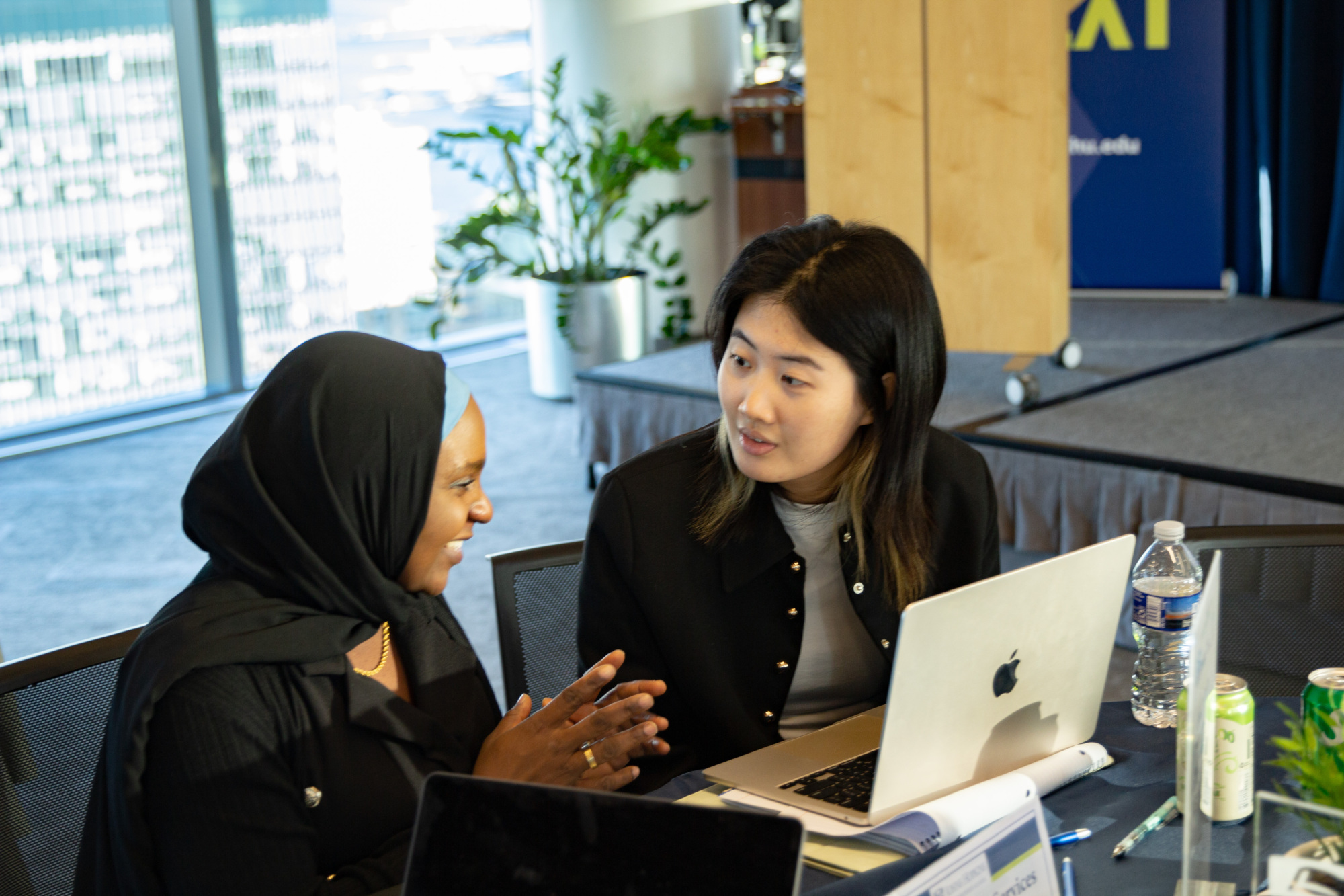 two people sitting at a table working on one laptop talking to each other