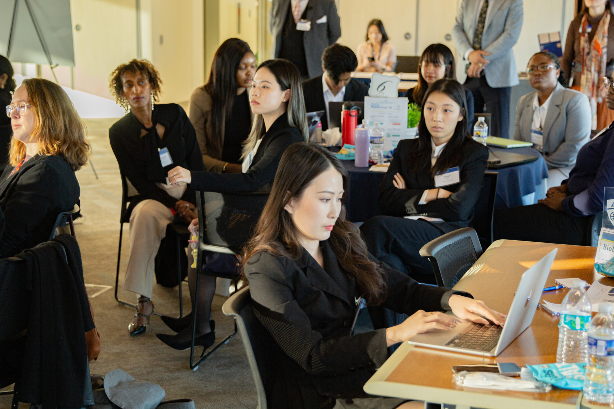 people sitting at tables, some working on laptops and some looking at the front of the room