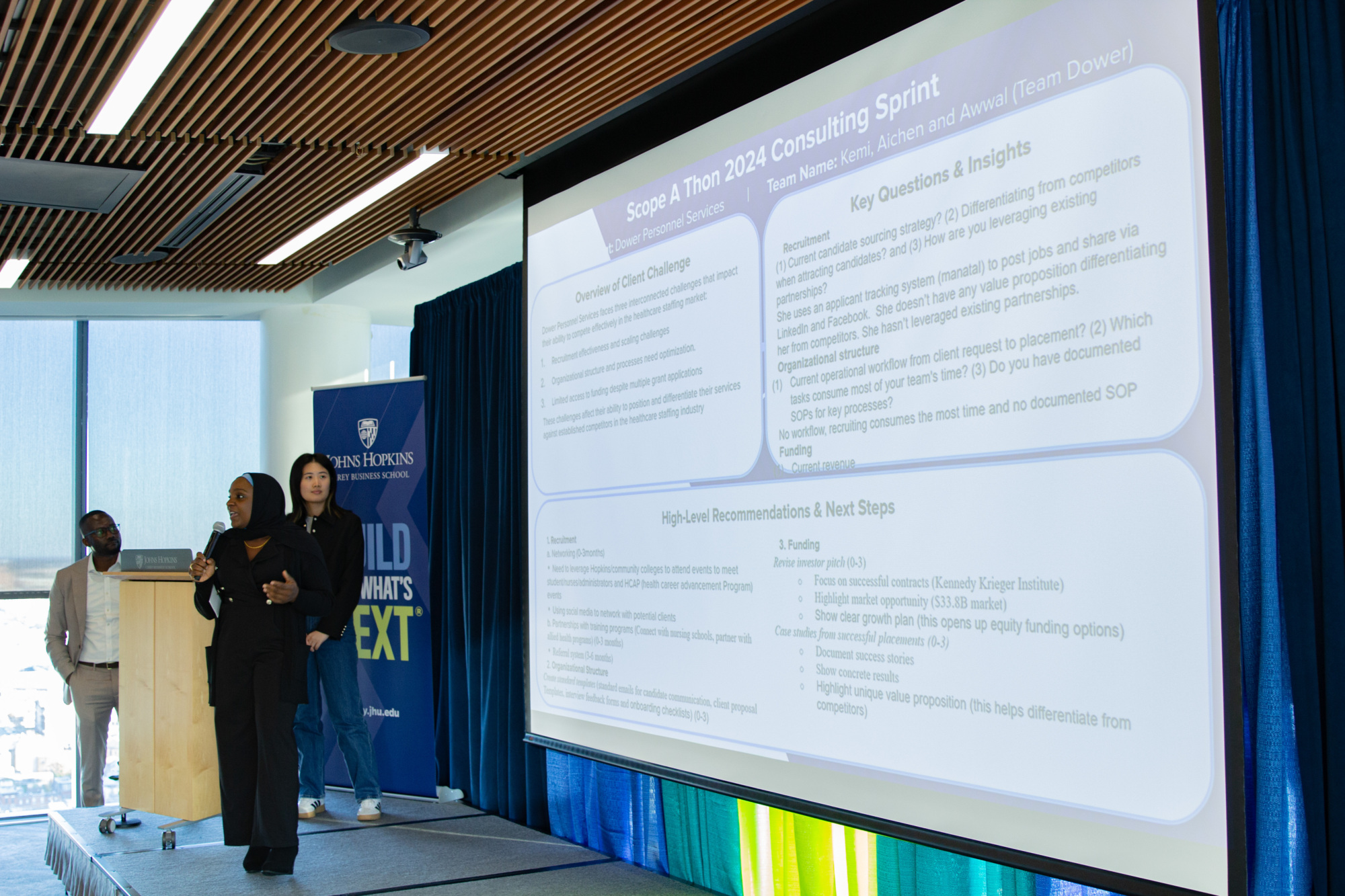 person standing on a stage presenting with a large projector with a presentation next to them