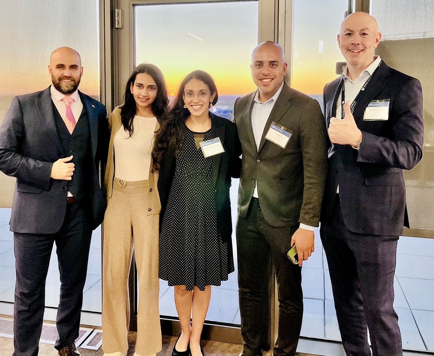 five people standing posing for a photo. one person has their thumbs up